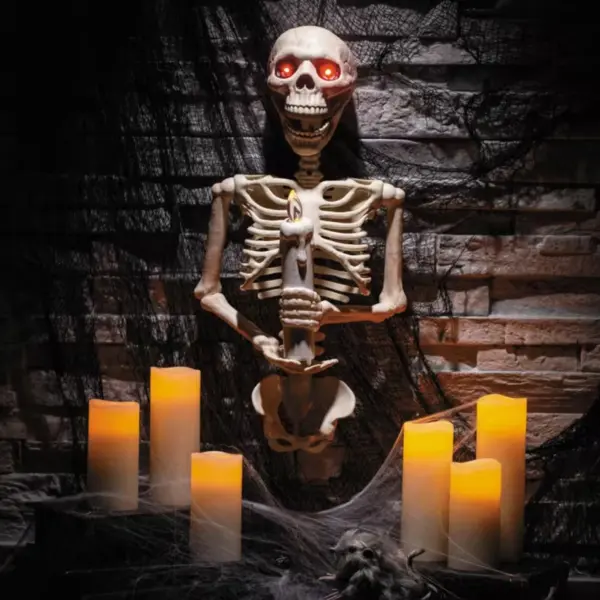 Ein dekoratives Halloween-Skelett mit leuchtenden Augen, das eine leuchtende Kerze hält.