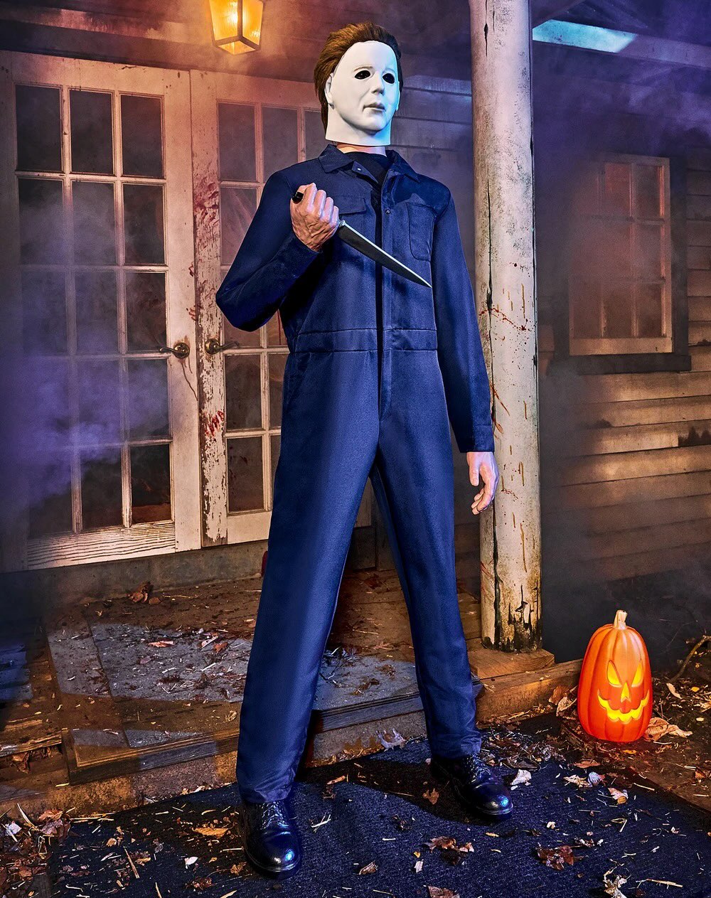 Spirit Halloween Michael Myers animatronic raising a knife in a dark lit scene beside a carved pumpkin