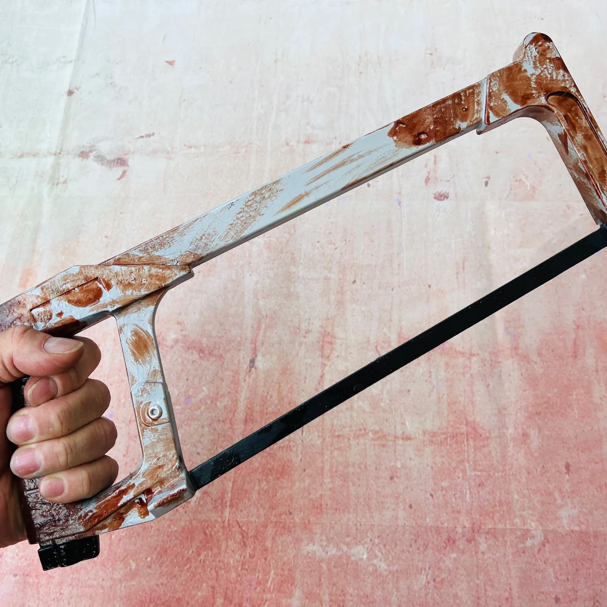 A hand holding a blood-covered hacksaw prop against a blood-stained backdrop